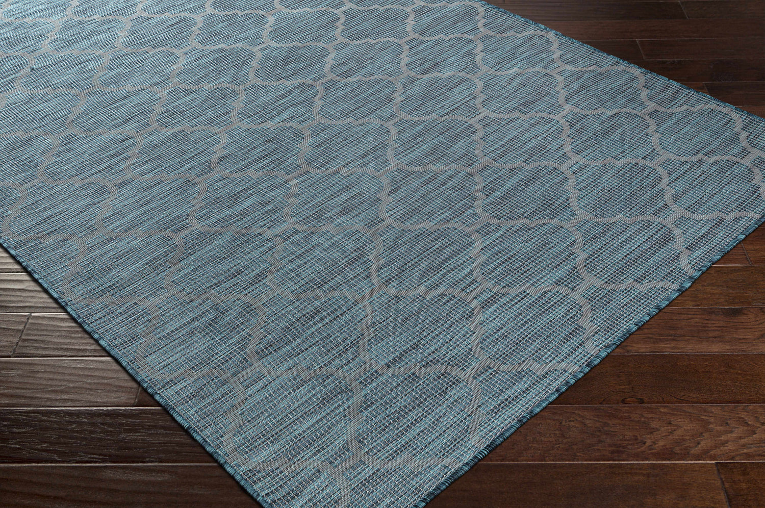 Close-up of Unique Outdoor Trellis Area Rug, Teal. Aqua rug with a black trellis pattern on dark wood floors. Corner