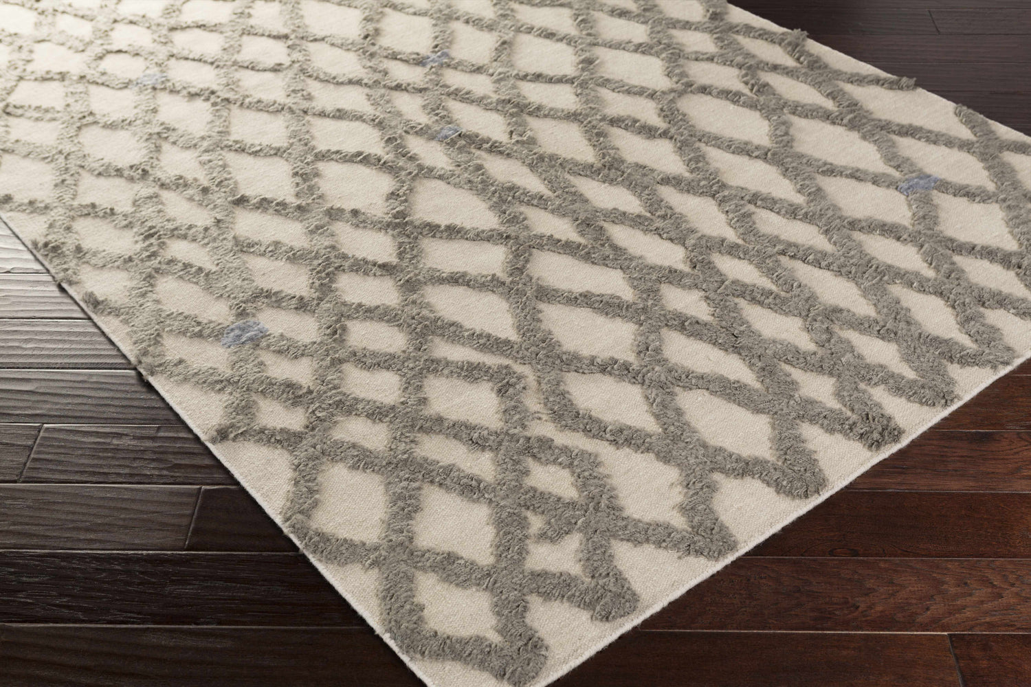 Close-up of Clare Area Carpet. Hand-woven wool shag rug in charcoal and medium gray with geometric lattice design. Corner