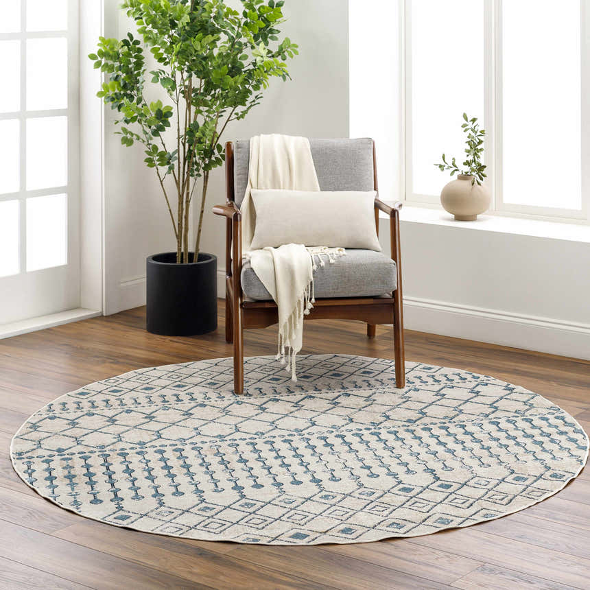 Living room scene with a round Cabognon Washable Area Rug in light beige and blue under a gray chair with a throw and pillow. Roomscene-Round