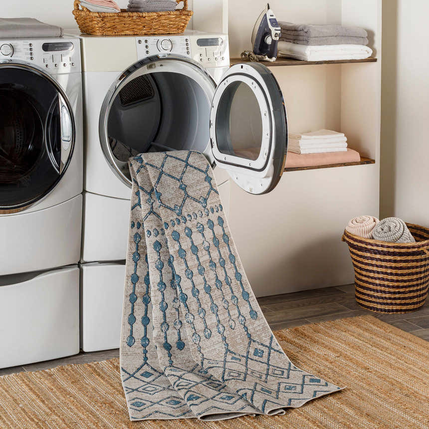 Laundry room scene with a blue and beige Cabognon Washable Area Rug coming out of the dryer. Jute rug on the floor. Washing-Machine