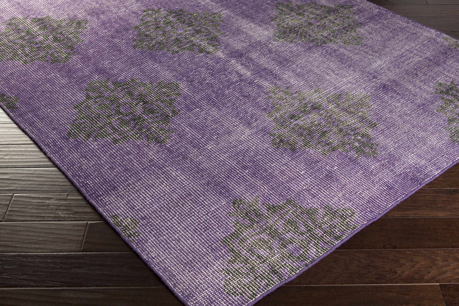 Close-up of the hand-knotted Camak Area Rug. 100% wool rug in medium purple with a black floral pattern. Corner