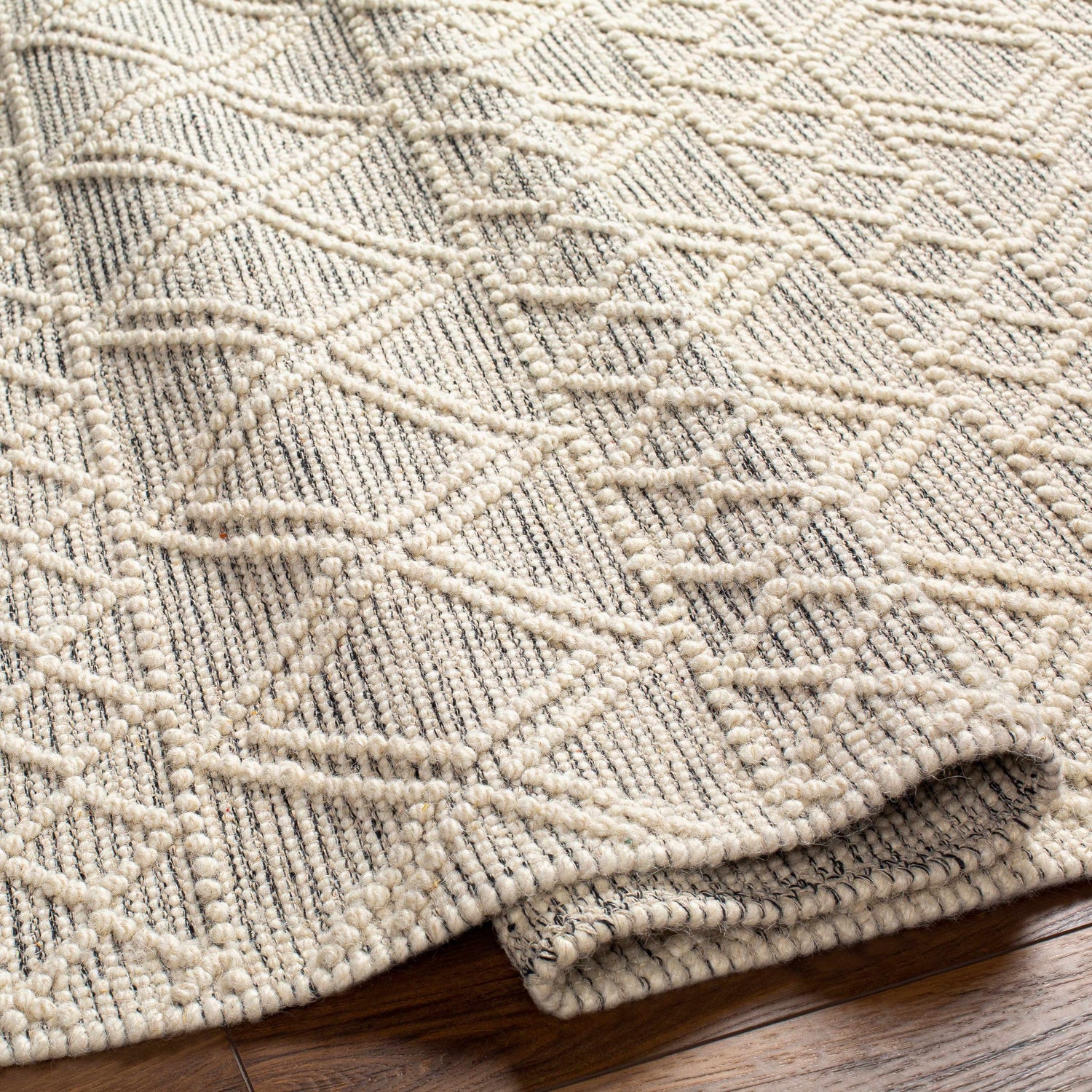 Close up of the Cameo Scandi Wool Rug showing bone and gray geometric pattern and hand woven texture. Fold