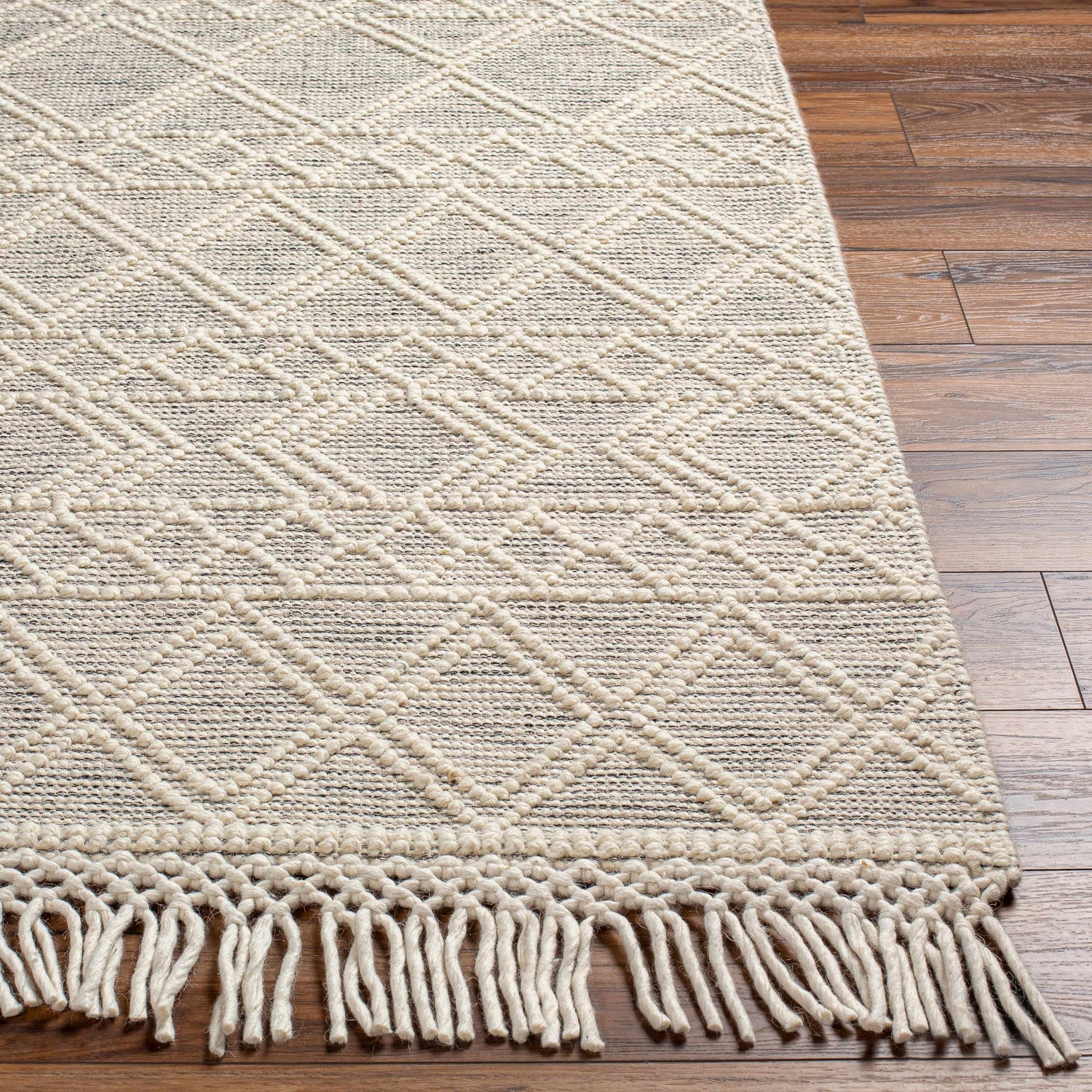 Close up of Cameo Scandi Wool Rug in bone color with geometric pattern and fringe detail on wood floor. Front