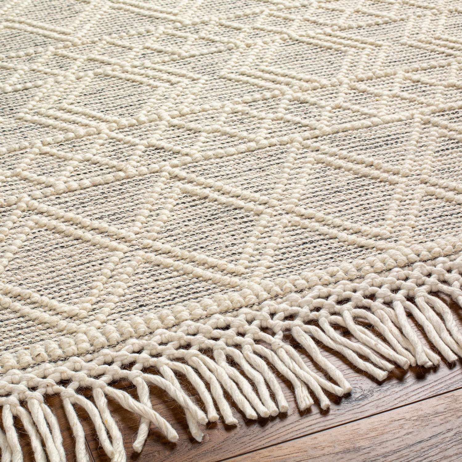 Close-up of Cameo Scandi Wool Rug in bone. Features geometric pattern, hand-woven texture, and knotted fringe detail. Texture