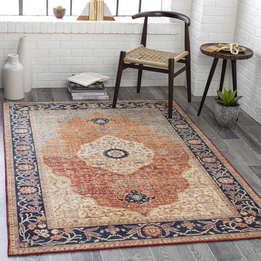 Living room scene with burnt orange Camperdown Area Rug, dark blue floral border, wood chair, and white brick wall. Roomscene-Rectangle