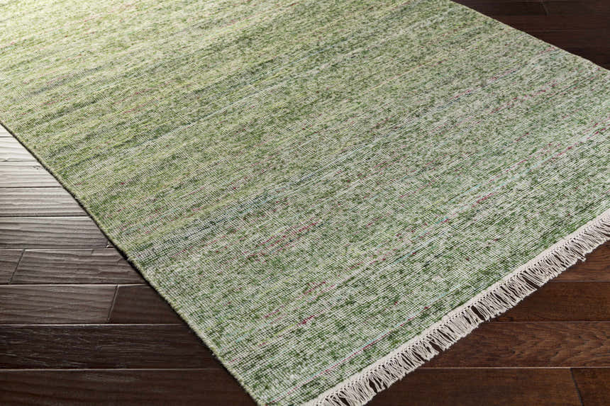 Close-up of a green Campti Area Carpet with ivory fringe on dark wood floors. Wool and viscose contemporary rug. Corner
