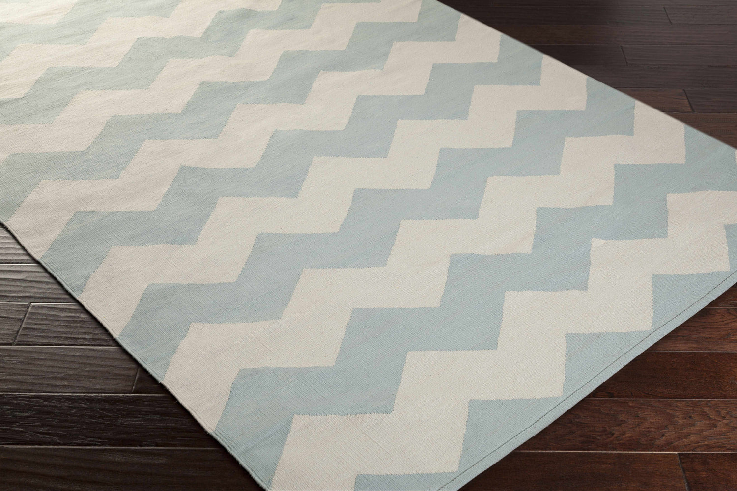 Close-up of the Caswell Area Rug in ice blue and ivory chevron pattern on dark wood floors. Hand woven cotton rug. Corner