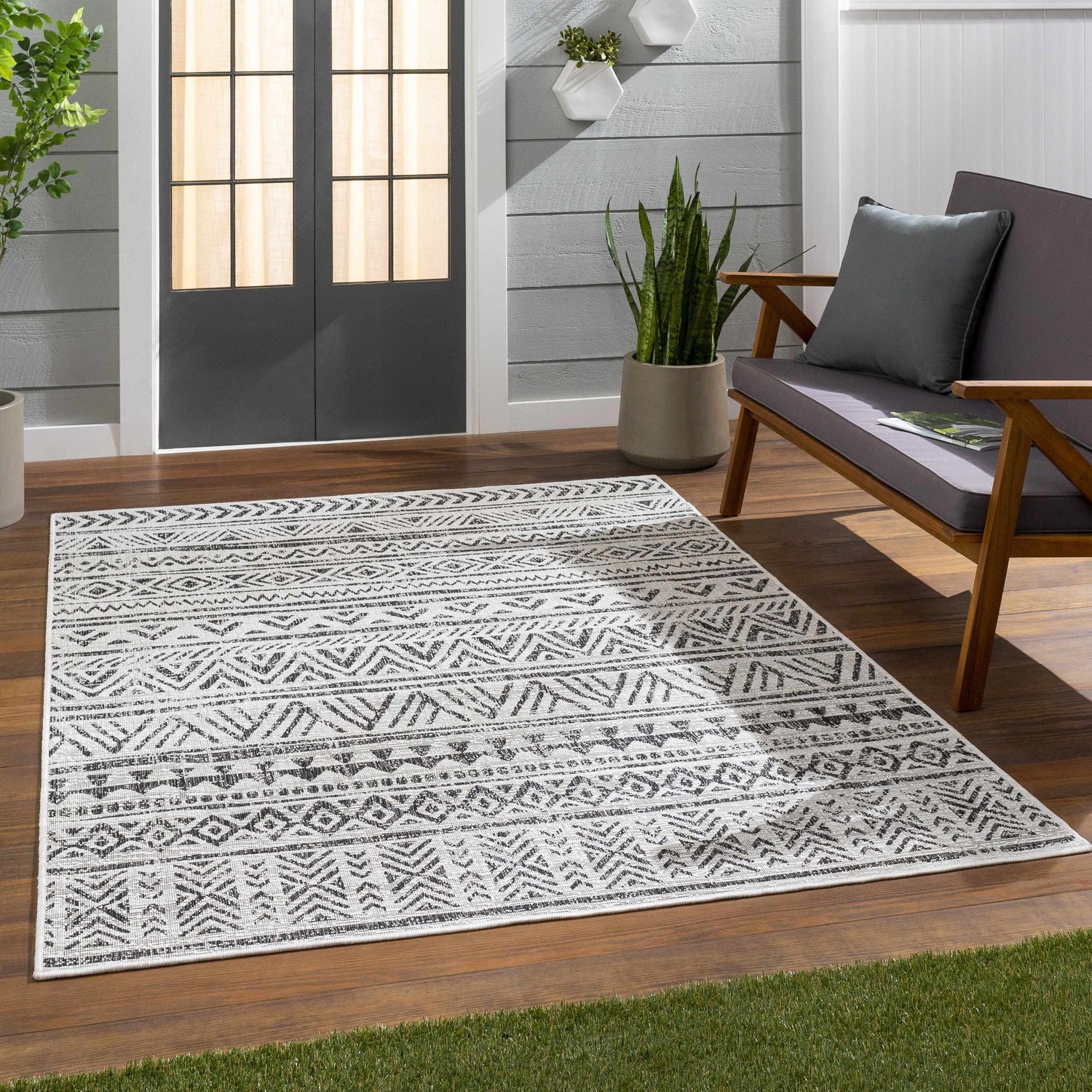 Outdoor patio scene with a black and white Bohemian Catrine Indoor & Outdoor Rug, gray loveseat, and wood flooring. Roomscene-Rectangle