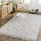 Living room scene with gray Cauldwell rug. Geometric, high/low pile rug with tassels styled with wood cabinet and chair. Roomscene-Rectangle