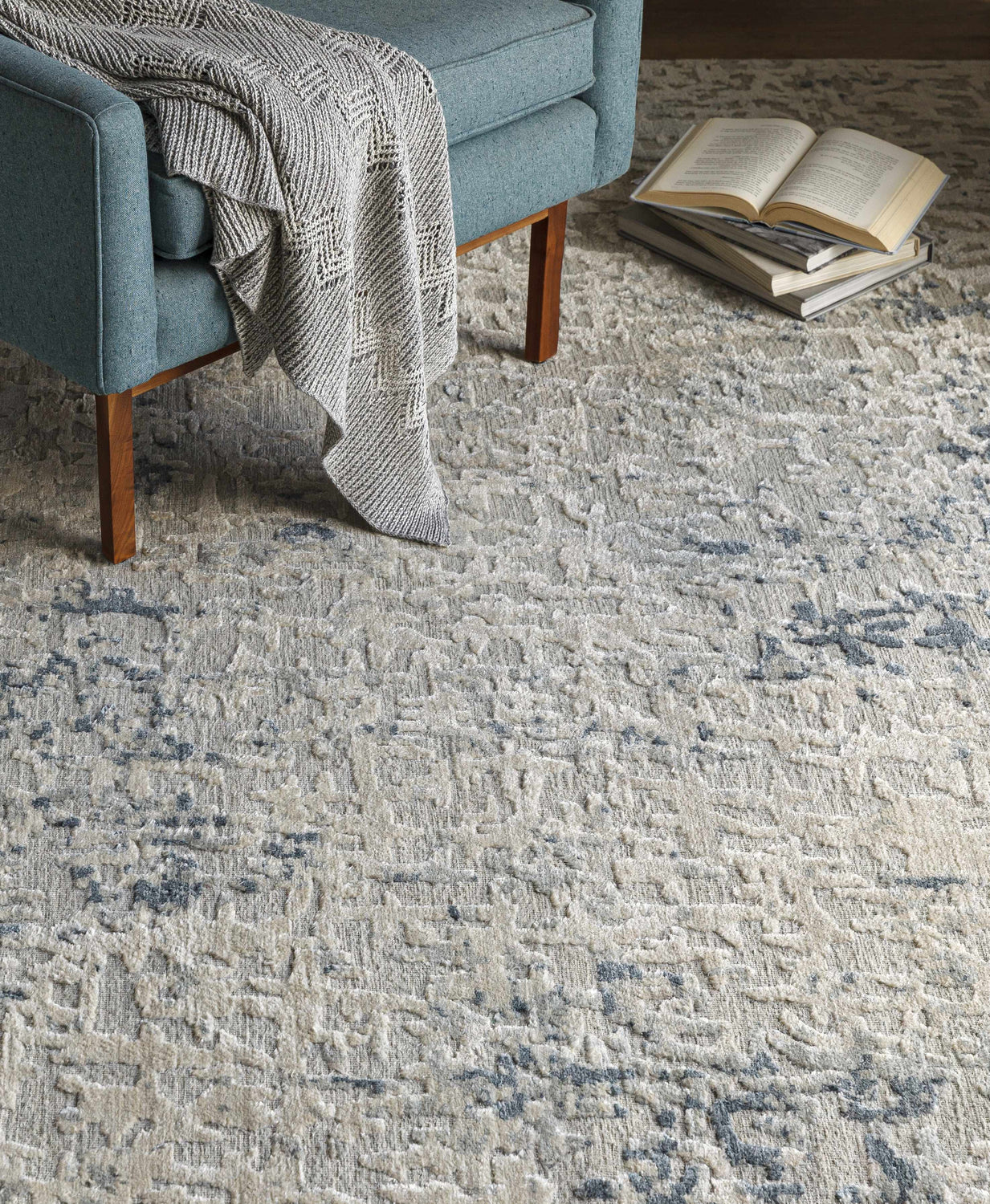 Living room scene with a blue chair, books, and the Cayuga Area Rug in off white and dark blue. Styleshot