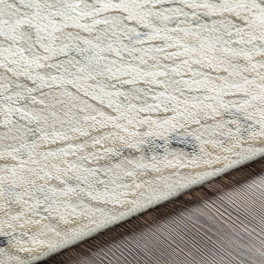 Close-up of the hand-knotted Cayuga Area Rug. Off-white silk rug with a subtle geometric pattern and dark blue and sage accents. Fold
