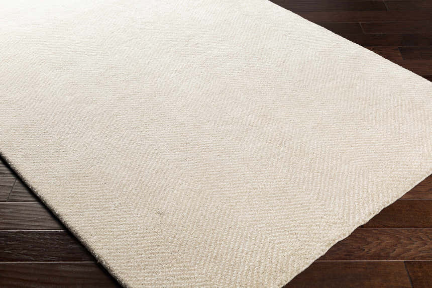 Close-up of the Ceiba Carpet, a hand-knotted rug in beige and ivory, showing its texture on dark wood floors. Corner