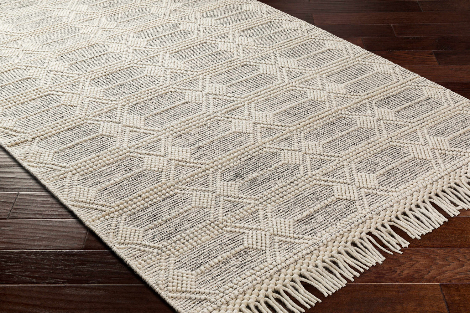 Close up of the Chars Wool Rug with tassels, bone color, geometric pattern, on dark wood floor. Corner