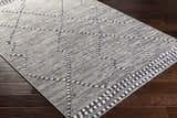 Close-up of the Cheverly Area Rug showing a gray, black, and white geometric pattern on dark wood flooring. Corner