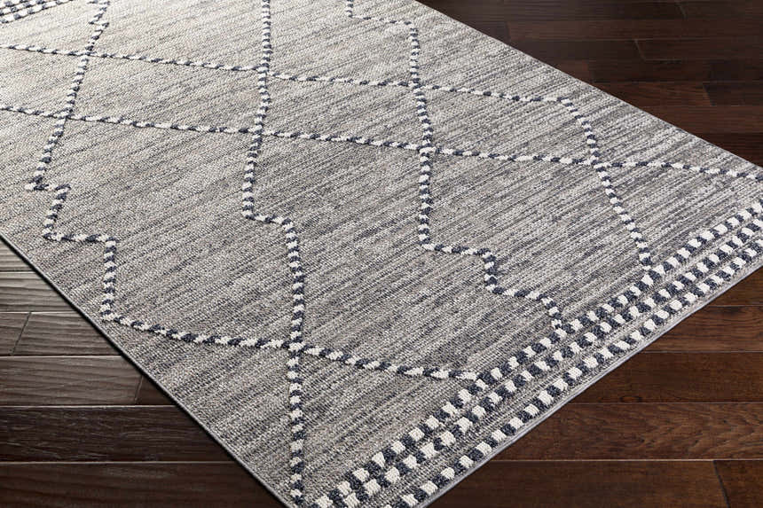 Close-up of the Cheverly Area Rug showing a gray, black, and white geometric pattern on dark wood flooring. Corner