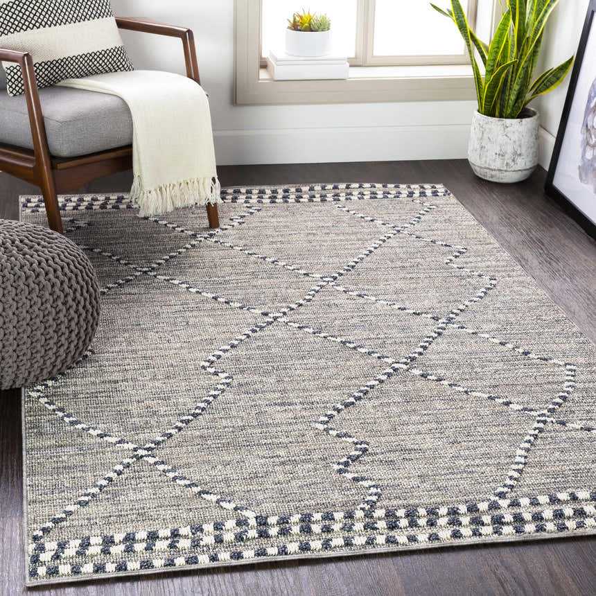 Living room scene with gray chair, pouf, and Cheverly Area Rug in black, gray, and white. Bohemian style. Roomscene-Rectangle