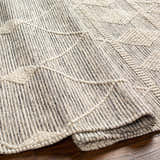Close-up of the geometric pattern and texture of the Hemingway Wool Rug in bone and gray. Hand-woven rug on hardwood floor. Fold