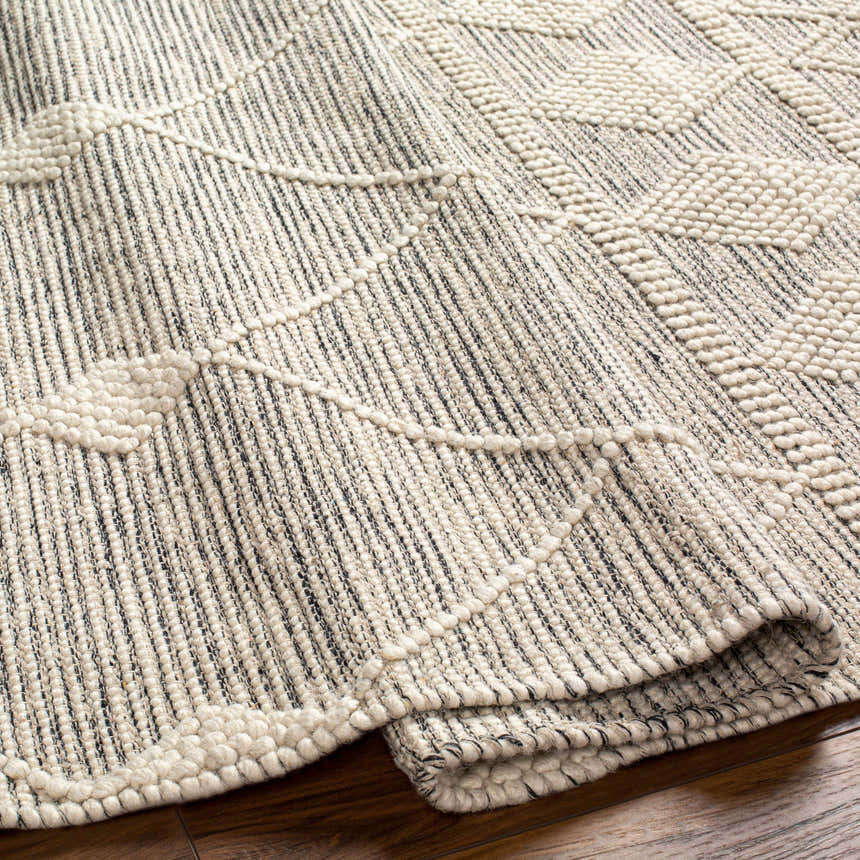 Close-up of the geometric pattern and texture of the Hemingway Wool Rug in bone and gray. Hand-woven rug on hardwood floor. Fold