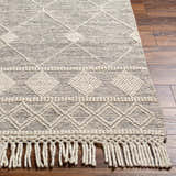 Close-up of the hand-woven Hemingway Wool Rug with Tassels. Bone and cloud gray geometric pattern and tassel fringe detail. Front