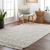 Neutral living room with a bone-colored Hemingway Wool Rug with Tassels, woven chair, and wood accents. Roomscene-Rectangle