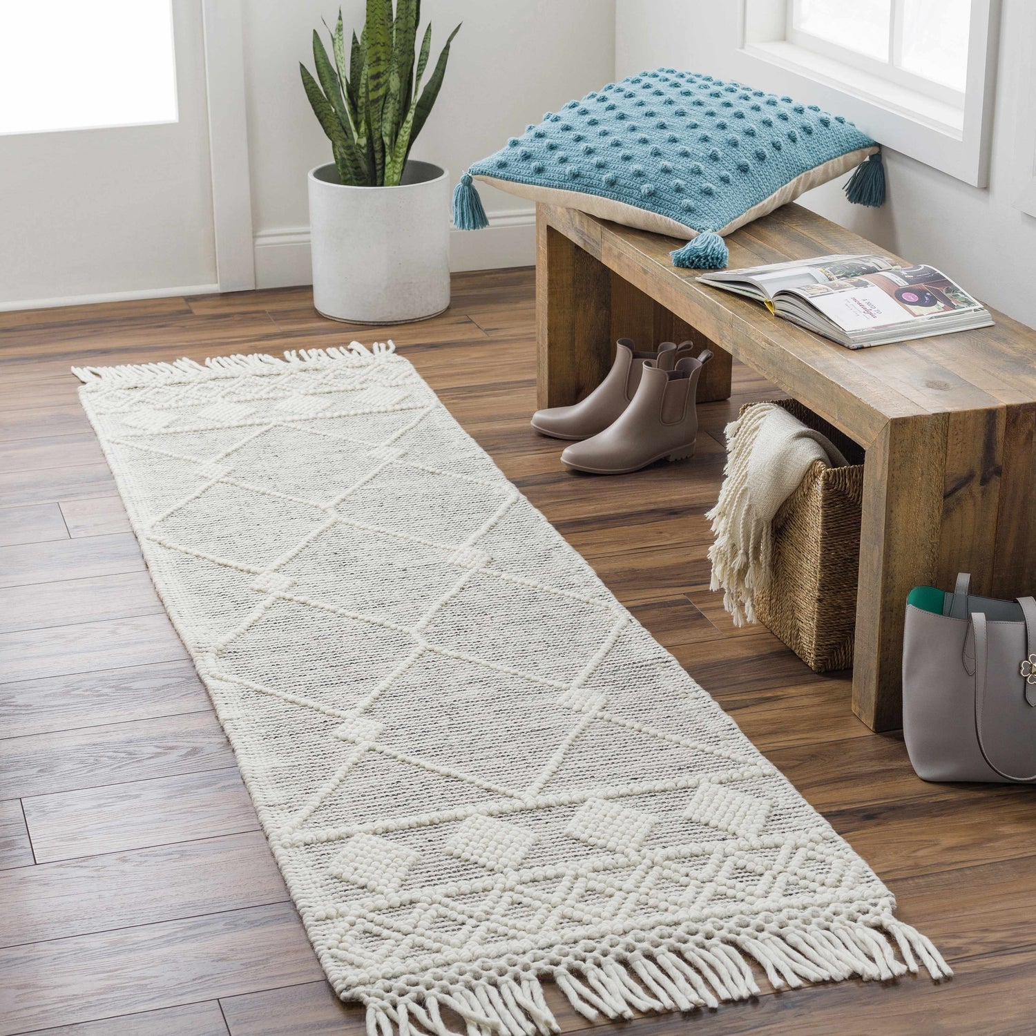 Entryway scene with a bone Hemingway Wool Rug with Tassels, wood bench, blue pillow, and wood floors. Roomscene-Runner