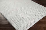Close-up of the cream Christoval Area Rug showing its hand woven texture and natural fibers on a dark wood floor. Corner