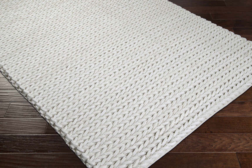 Close-up of the cream Christoval Area Rug showing its hand woven texture and natural fibers on a dark wood floor. Corner