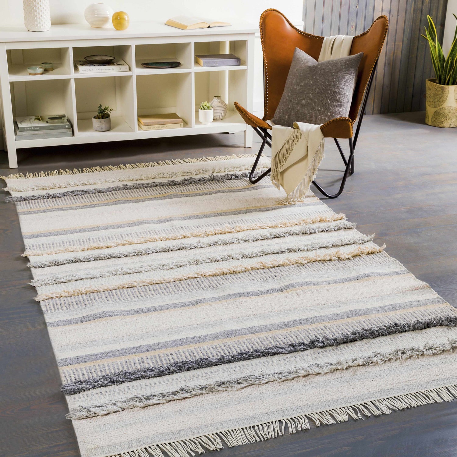 Living room scene with a Charlemagne Flatweave Performance Rug in charcoal, cream, and gray, styled with a leather chair and white shelving. Roomscene-Rectangle