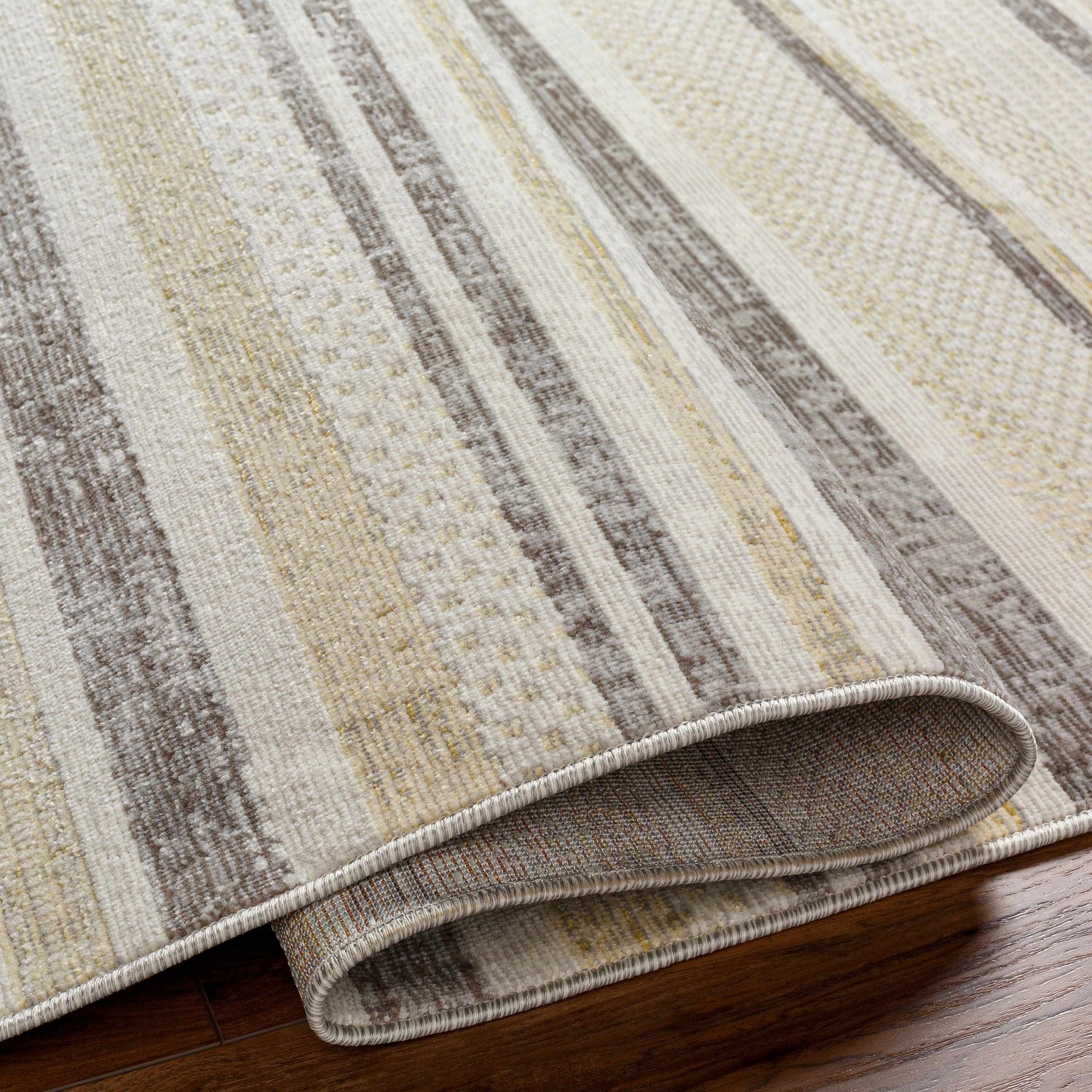 Close-up of Chato Area Rug with bone, gray, nutmeg, and white thatch stripes. Machine woven texture detail. Fold