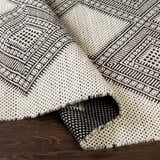 Close-up of the hand woven Claveria Area Carpet. Black and cream wool rug with bohemian geometric pattern and textured weave. Fold