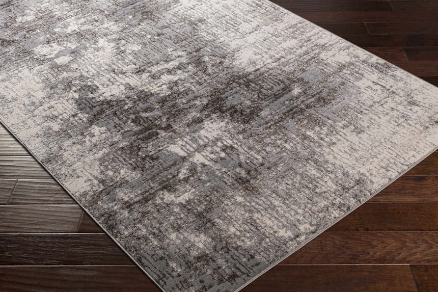 Close-up of the Calabasa Area Rug showing its charcoal, gray, and light gray contemporary pattern on dark wood floors. Corner