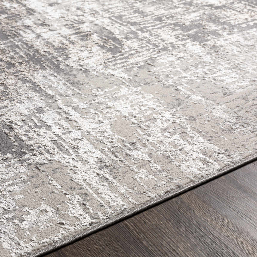Close-up of the charcoal, gray, and light gray abstract design of the Calabasa Area Rug on dark wood flooring. Texture