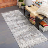 Entryway scene with a gray Concordia Faux Silk Rug, woven bench, plants, books, and a decorative pillow. Roomscene-Runner