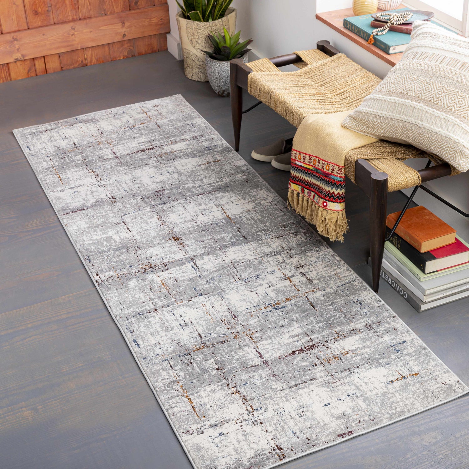 Entryway scene with a gray Concordia Faux Silk Rug, woven bench, plants, books, and a decorative pillow. Roomscene-Runner