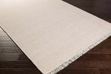 Close-up of the hand-knotted Collydean Area Rug in camel and ivory with fringe detail on dark wood floors. Corner