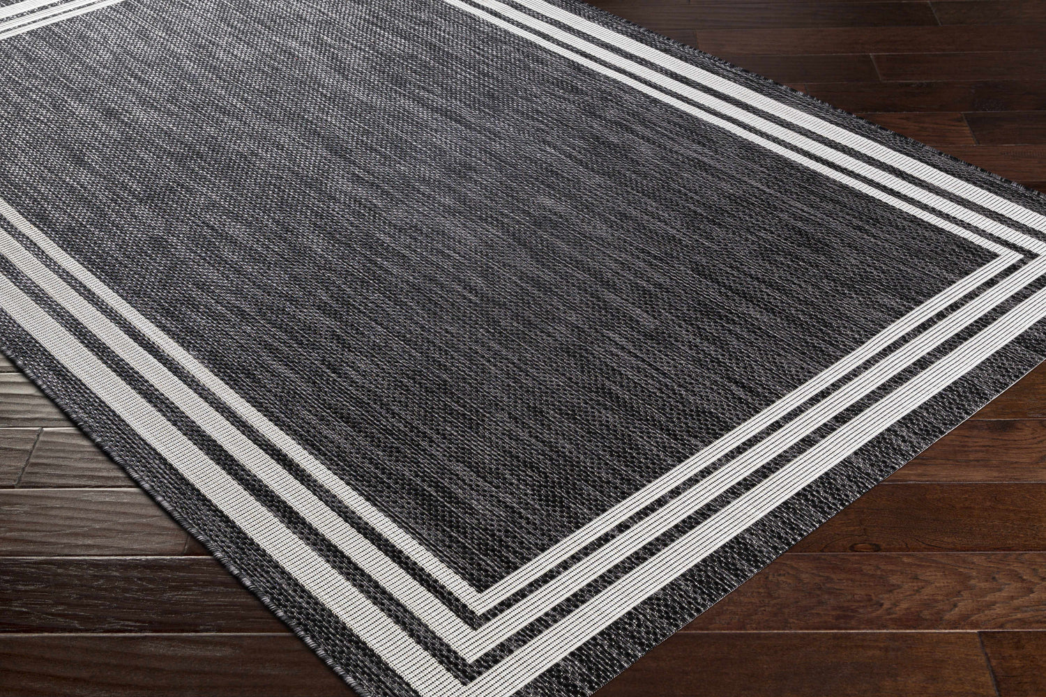 Close-up of the Coonamble Bordered Antrasit Rug. Charcoal rug with a cream striped border on dark wood floors. Corner