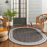 Cozy porch scene with an oval Coonamble Bordered Antrasit Rug, wicker chairs, wood floors, and a potted plant. Roomscene-Oval
