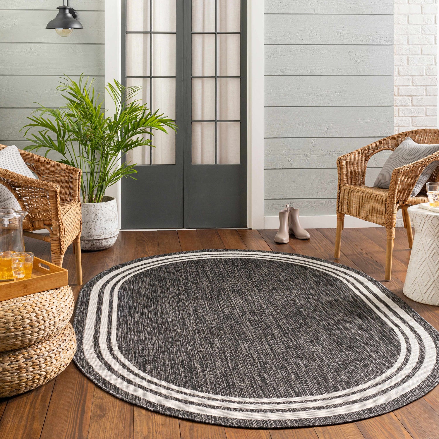 Cozy porch scene with an oval Coonamble Bordered Antrasit Rug, wicker chairs, wood floors, and a potted plant. Roomscene-Oval
