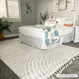 Coastal bedroom scene with a Dauin 3D Rainbow Area Rug in cloud gray, cream, and gray tones with tassels. Roomscene-Rectangle