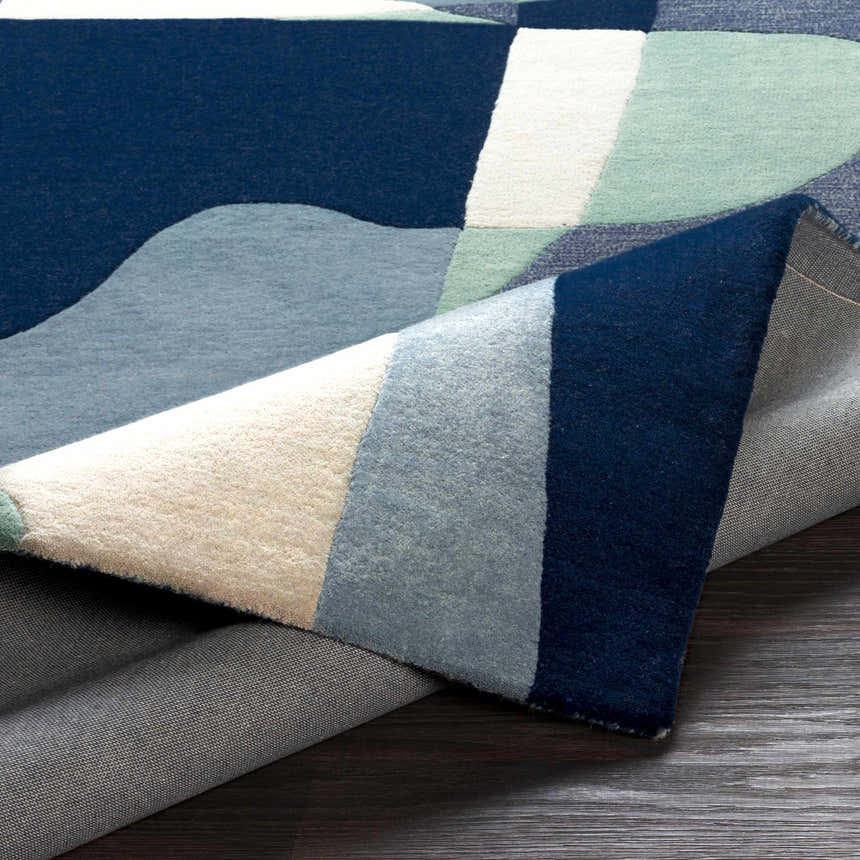 Close up of the Crawfordsville rug showing its hand tufted wool texture and modern geometric design in blue, sage, and oatmeal. Fold