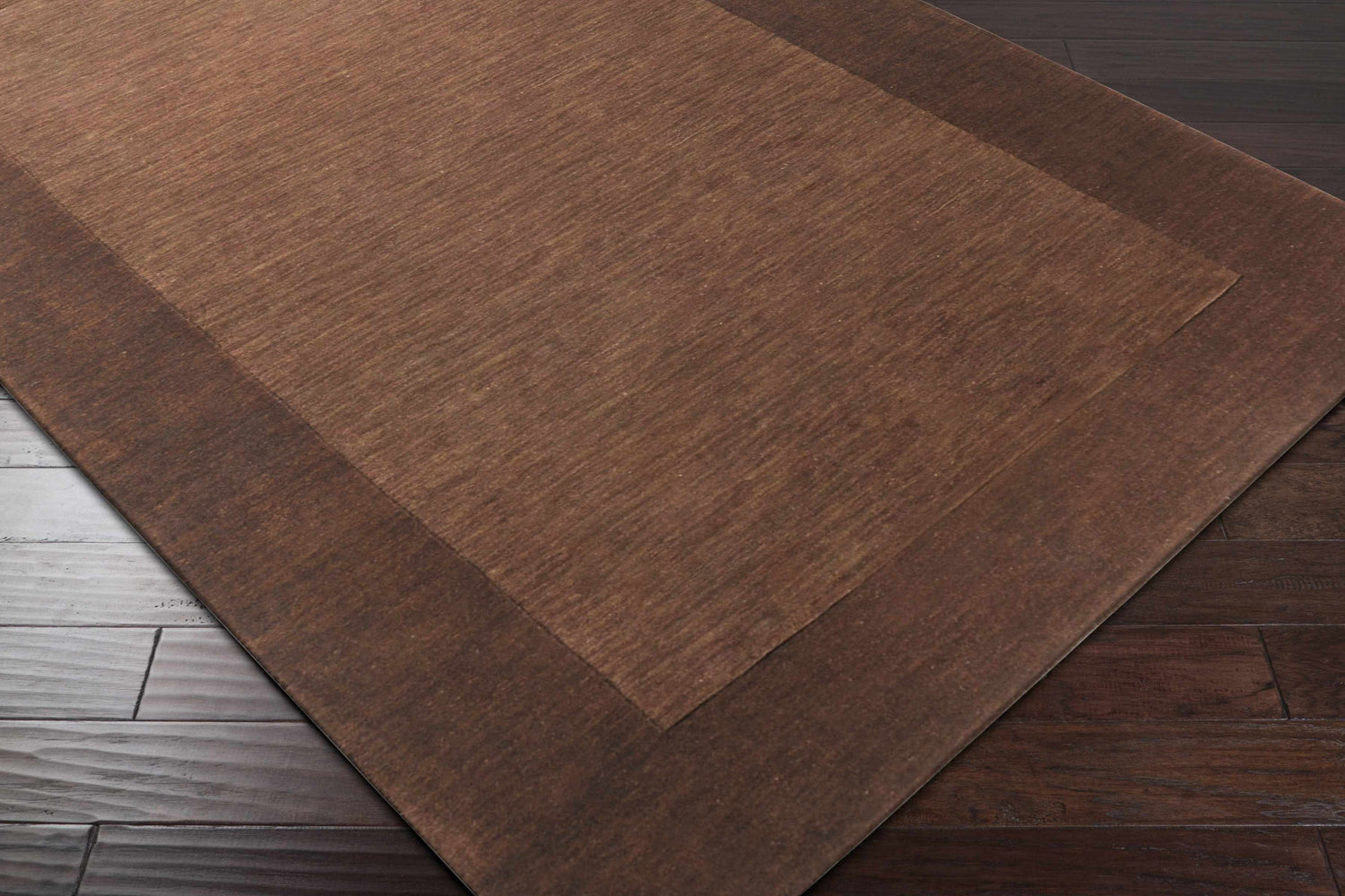 Close-up of a Bordered Solid Brown Wool Rug showing texture and color variations on dark wood floor. Corner