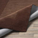 Close-up of a Bordered Solid Brown Wool Rug showing the dark brown color, border detail, and the rug's backing. Fold