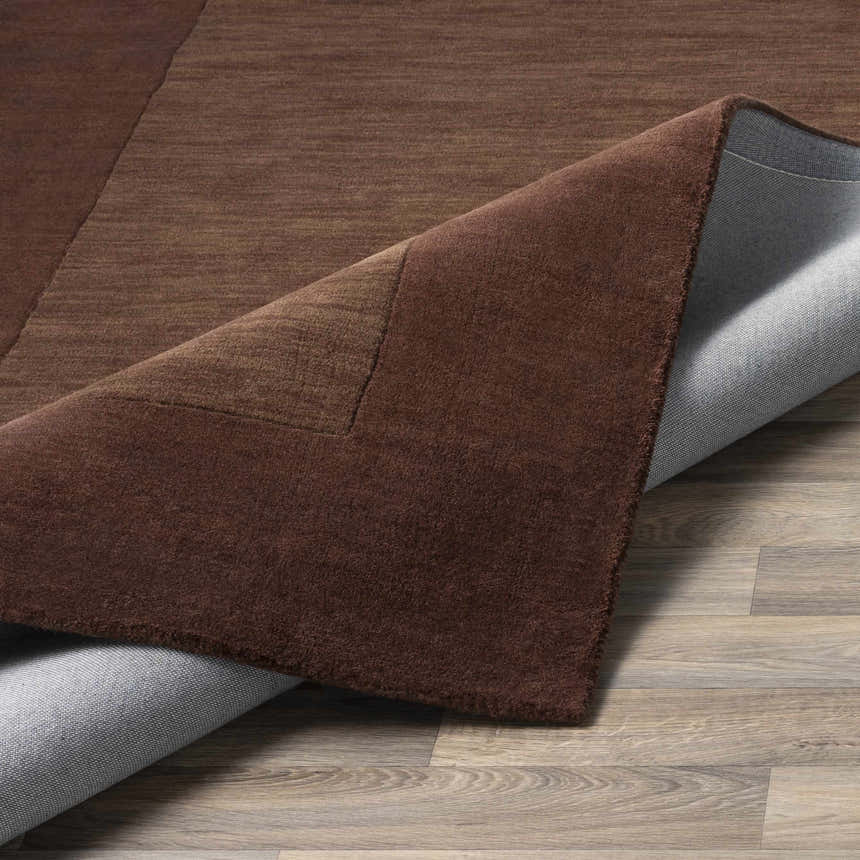 Close-up of a Bordered Solid Brown Wool Rug showing the dark brown color, border detail, and the rug's backing. Fold