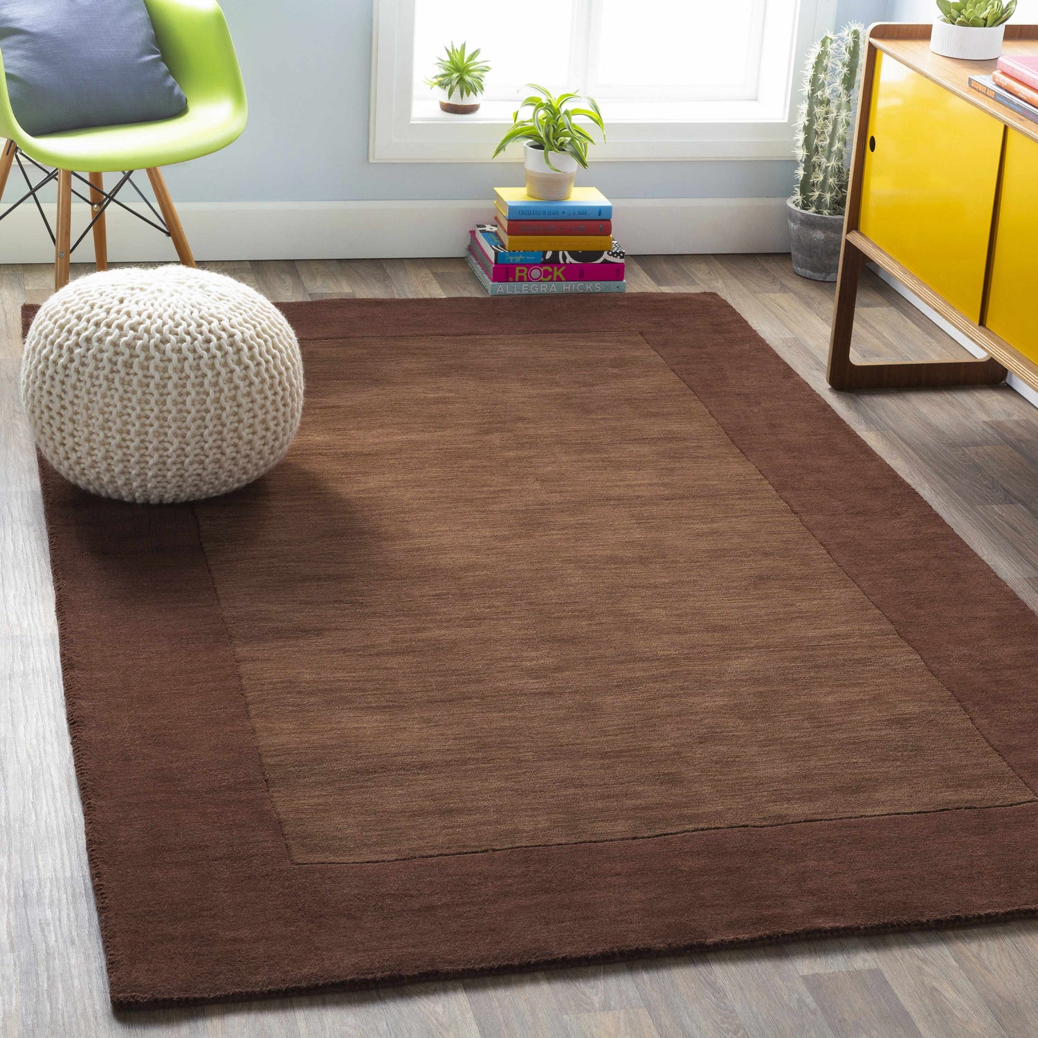 Living room scene with a Bordered Solid Brown Wool Rug, white pouf, green chair, and yellow cabinet. Roomscene-Rectangle