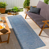 Outdoor patio scene with a blue Corlette Area Rug, wooden furniture, plants, and gardening tools. Roomscene-Runner