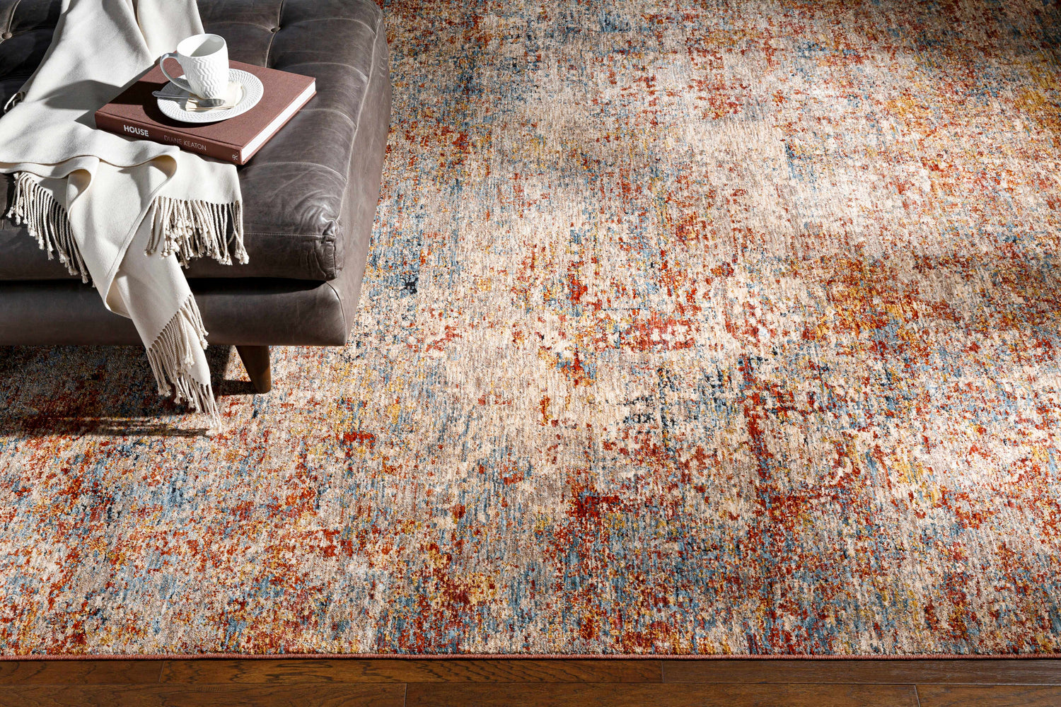 Living room scene with a Cranfield Area Rug in brick red, cream, blue, and brown tones, styled with a leather couch and wood floors. Styleshot