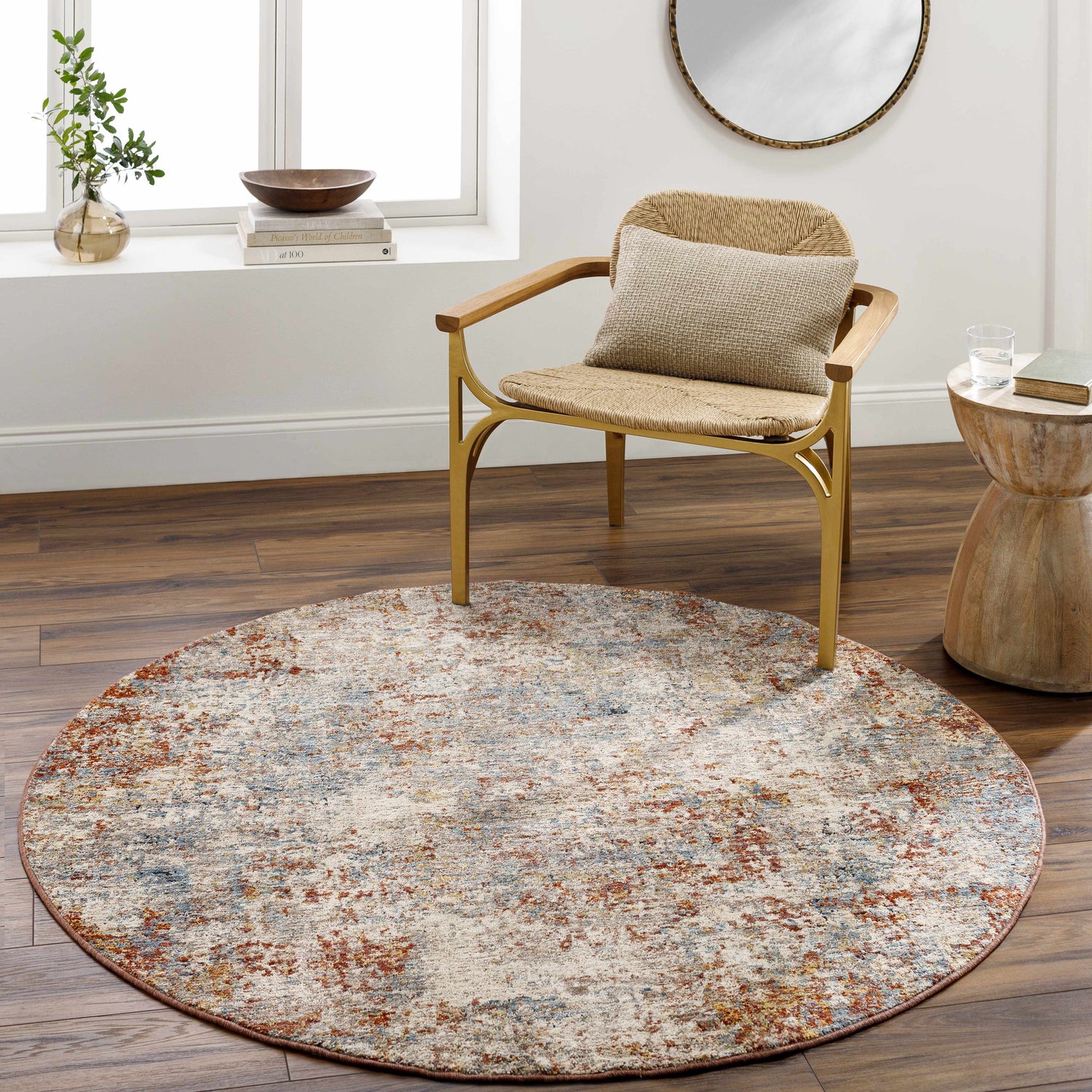 Living room scene with a round Cranfield Area Rug in brick red, cream, and blue under a chair on wood floors. Roomscene-Round