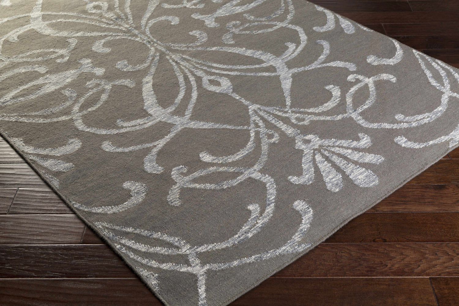 Close-up of the Cottekill Area Rug. Brown wool rug with an off-white, contemporary floral pattern on dark wood floors. Corner
