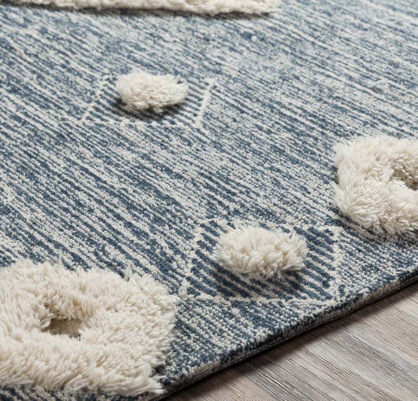 Close up of Curllsville Area Rug showing cream pom poms on a textured navy and cream, hand-tufted wool rug. Texture