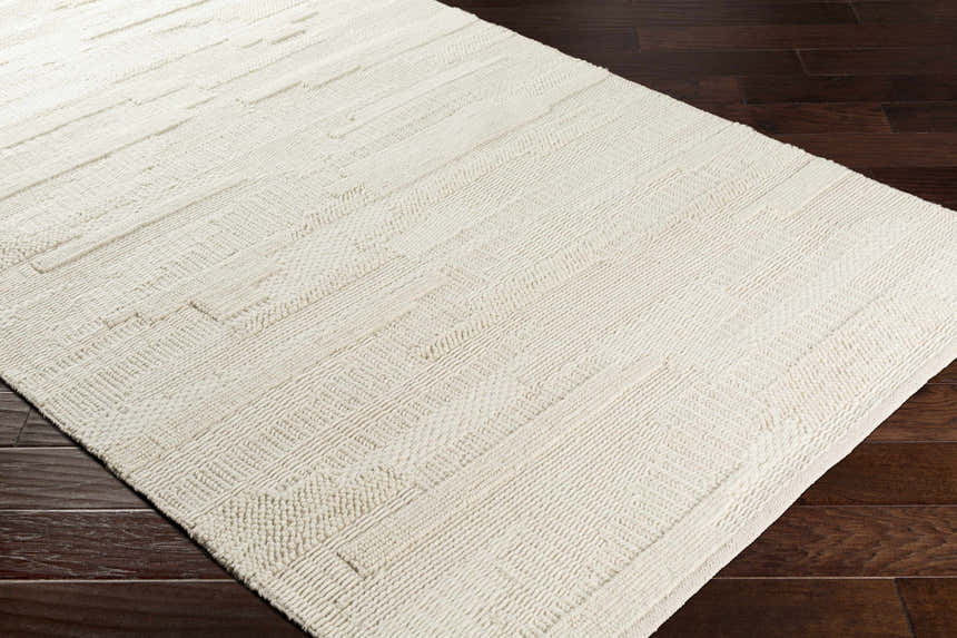 Close-up of the Cypress Cream Textured Wool Rug showing its woven design and soft, neutral color on dark wood floor. Corner